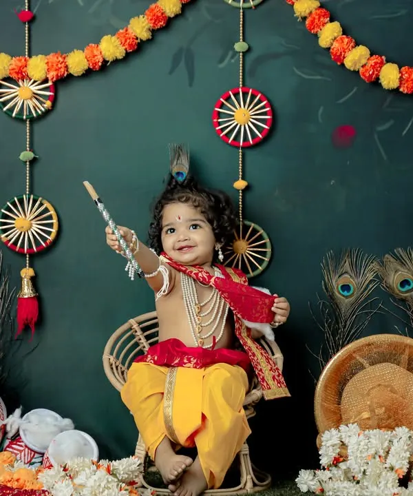 A joyful little Krishna celebrating Janmashtami in our studio. The vibrant backdrop with peacock feathers and marigolds creates a festive atmosphere for this divine photoshoot.
