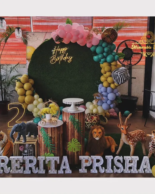 A complete jungle theme birthday party setup, featuring a lush green backdrop, a custom 'Happy Birthday' sign, wood-textured plinths, and a variety of friendly animal props to create a wild adventure.