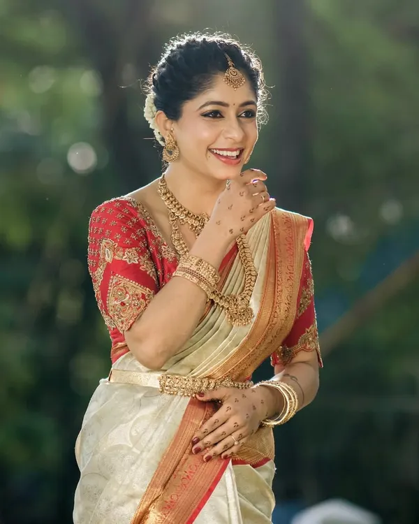 This bride looks radiant in a classic red and cream Kanjivaram saree. I designed a matching red blouse with rich gold embroidery on the sleeves and a modern transparent back, blending tradition with a contemporary touch.