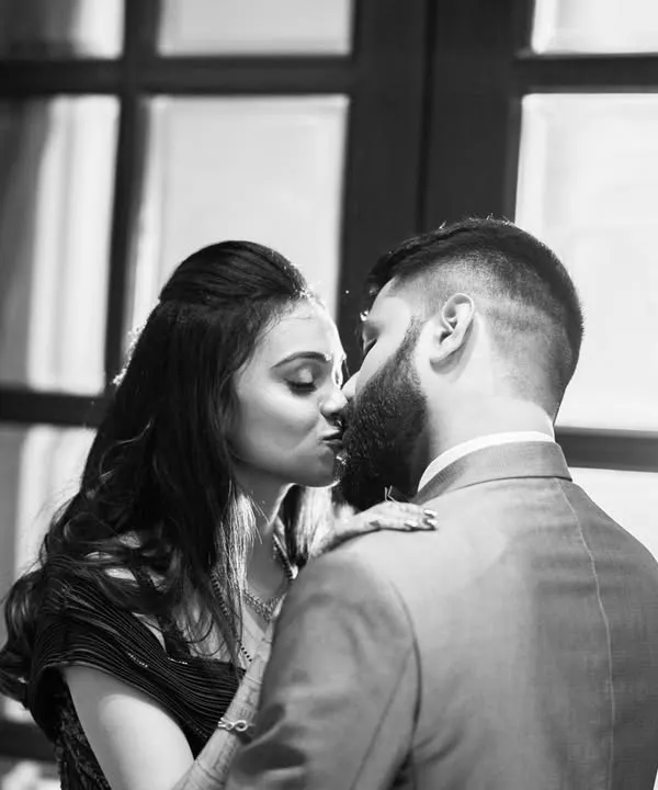 An intimate black and white portrait, capturing a kiss against a beautifully lit window. Monochrome enhances the romance and timelessness of the moment.