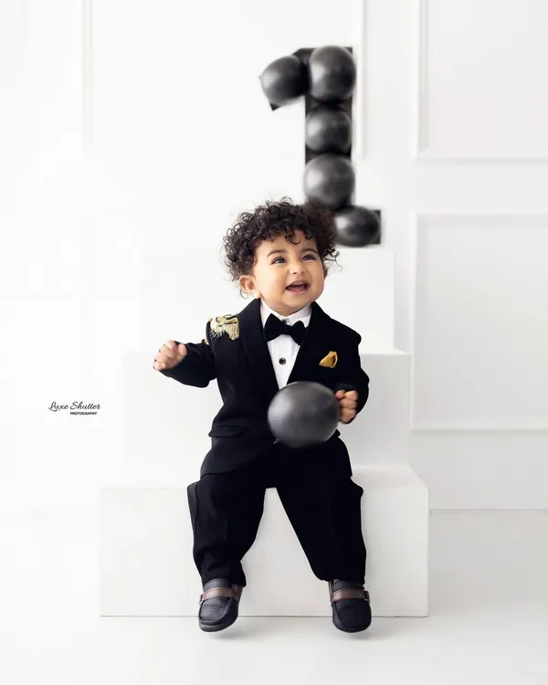 A stylish first birthday portrait. This little boy with amazing curls looks so charming and happy in his black tuxedo, ready to celebrate turning one.