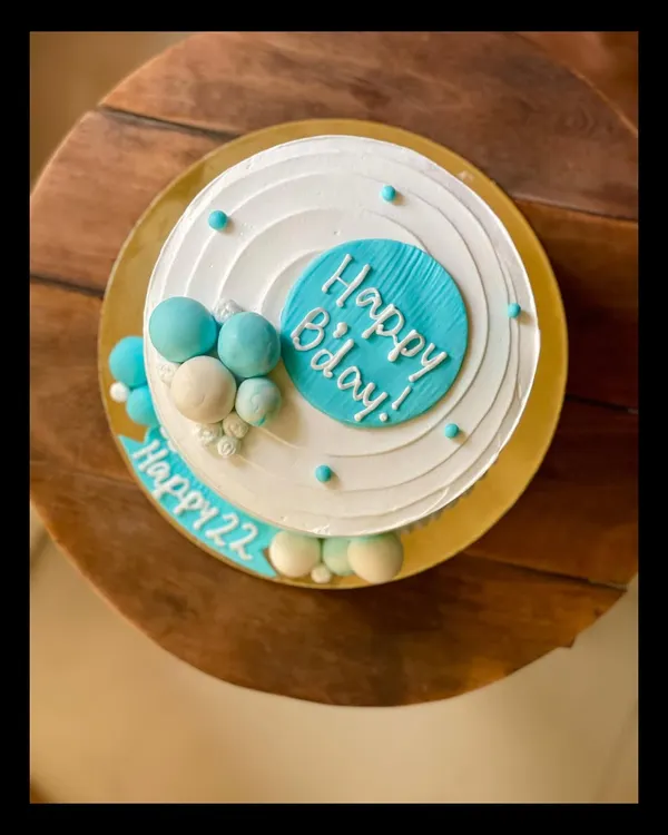 A minimal and modern birthday cake in shades of blue and white, decorated with chocolate spheres.