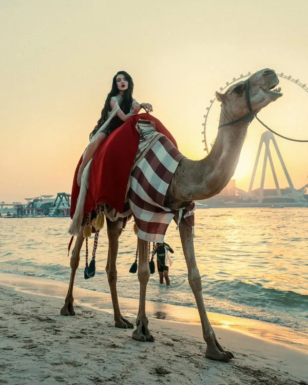 Where the desert meets the waves, she reigns. A breathtaking sunset portrait in Dubai, featuring a model on a camel with the Ain Dubai wheel in the background.