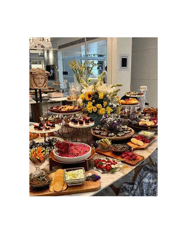 I treat every table as a canvas, creating a stunning, abundant centerpiece that invites your guests to gather and connect. This spread features a rich variety of textures and flavors, from artisanal cheeses and charcuterie to vibrant dips and fresh fruits, all beautifully arranged with floral accents.