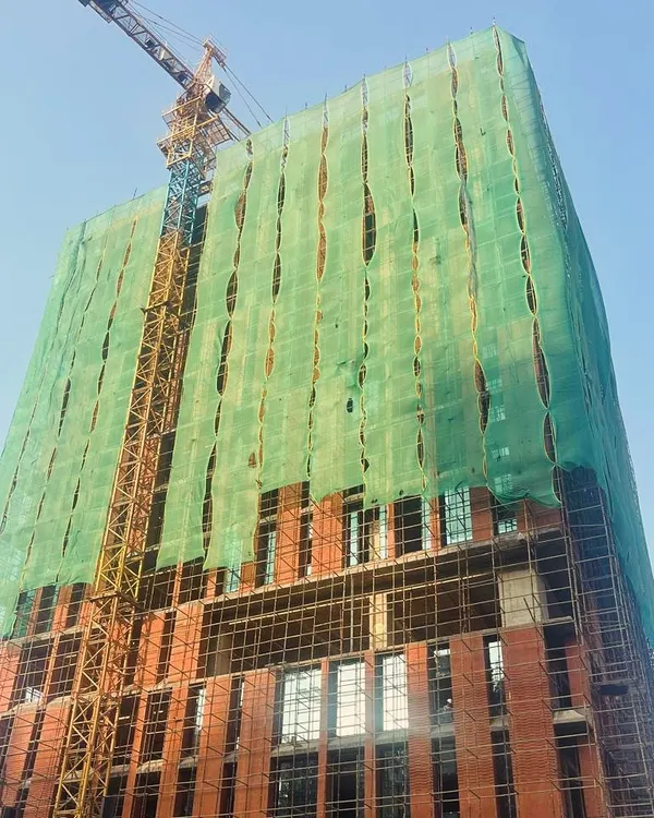 An office tower under construction, with its brick facade taking shape beneath the scaffolding. The green safety netting creates an unintentional, large-scale art installation, reminiscent of the work of Christo and Jeanne-Claude.