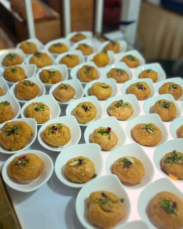 A display of a classic Indian sweet, perfectly portioned in individual white bowls and garnished with chopped nuts and rose petals. This presentation makes it easy for guests to enjoy at a large event.
