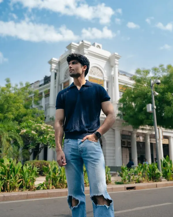A full-length outdoor shot of a model in casual ripped jeans and a polo shirt, set against classic architecture. This image showcases a confident, relaxed look for a lifestyle portfolio.