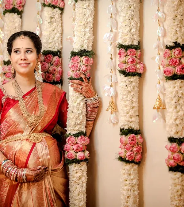 A beautiful solo portrait of the mom-to-be during her baby shower. Dressed in a stunning silk saree and traditional jewelry, she stands before an elegant floral backdrop.