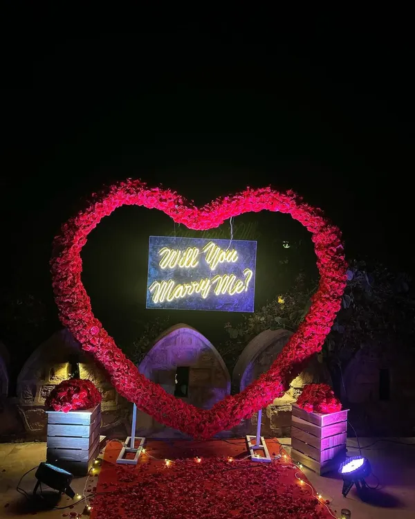 A breathtaking proposal setup featuring a massive heart-shaped arch made entirely of red roses. At the center, a "Will You Marry Me?" neon sign glows, creating an incredibly romantic and picture-perfect moment.
