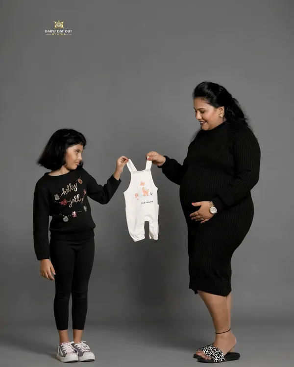 A sweet moment between a mother and daughter, looking forward to the new baby's arrival. Using a tiny baby outfit as a prop is a lovely way to announce the new addition to the family.