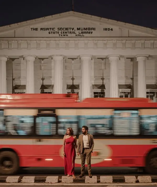 A classic Mumbai moment. The iconic red BEST bus adds a dynamic blur of color to this romantic shot in front of the Asiatic Society Library, creating a truly cinematic pre-wedding photograph.