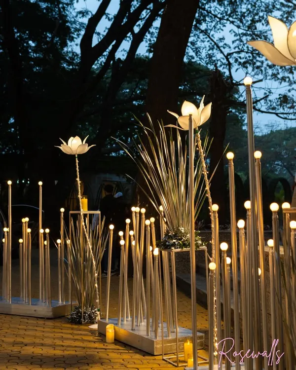 An enchanting entrance pathway created with illuminated lotus-shaped lights and tall grass elements, setting a magical tone for an evening celebration.