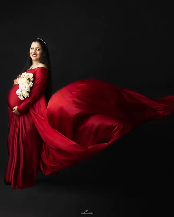 A dramatic studio portrait featuring a flowing red satin gown against a classic black backdrop, creating a powerful and elegant silhouette. This is one of our most requested fine art maternity photography styles.