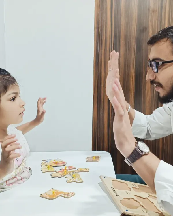 A therapist and child share a high-five after successfully completing a puzzle. This language therapy session incorporates fine motor practice, shape recognition, and positive reinforcement.