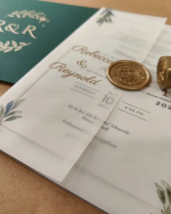 This bespoke wedding invitation features a printed vellum jacket, delicately wrapped and sealed with a luxurious gold wax seal. Paired with a deep glass glow green envelope, it's a perfect blend of timeless charm and contemporary style.