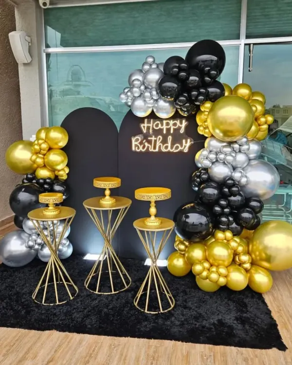 A glamorous black, gold, and silver balloon arch with a neon sign and matching cake stands. This setup is perfect for a sophisticated party on a terrace or patio.