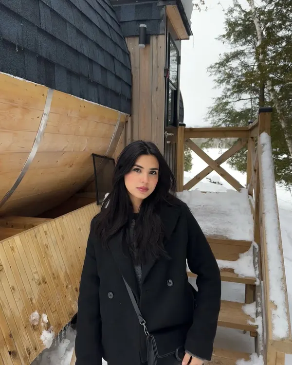 A classic winter portrait in an all-black outfit against a snowy cabin backdrop in Parry Sound.