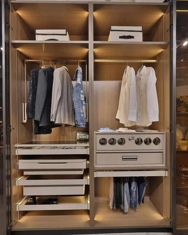 A look inside a perfectly organized wardrobe. This design features dedicated sections for hanging clothes, multiple pull-out drawers for folded items, and a specialized unit with circular displays, all illuminated by warm, integrated LED lighting.