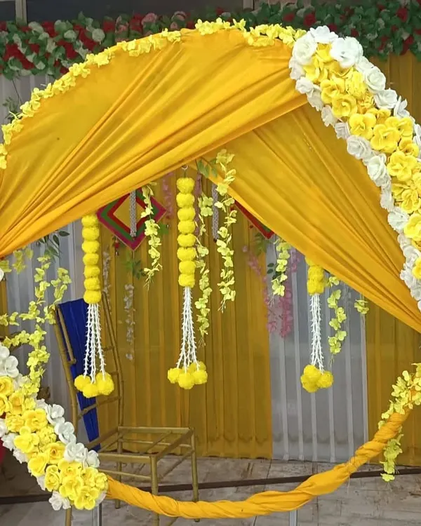 A close-up of a circular Haldi backdrop, showing how yellow fabric is draped within the frame and accented with marigold and white flower garlands.