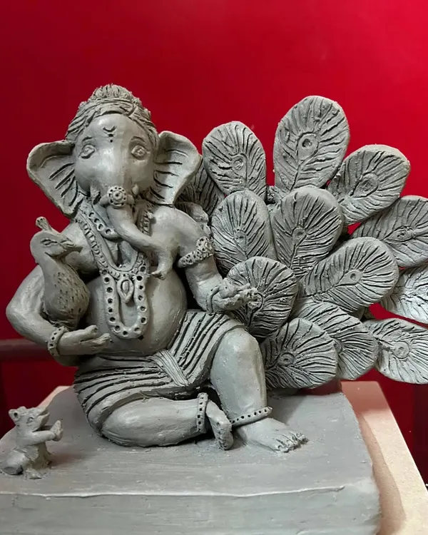 A full view of the 'Mayur Pankh' Ganesha, a custom-designed clay sculpture. Notice the intricate details on the feathers and the small mouse (mushak) at his feet, all handcrafted from natural Shadu clay.