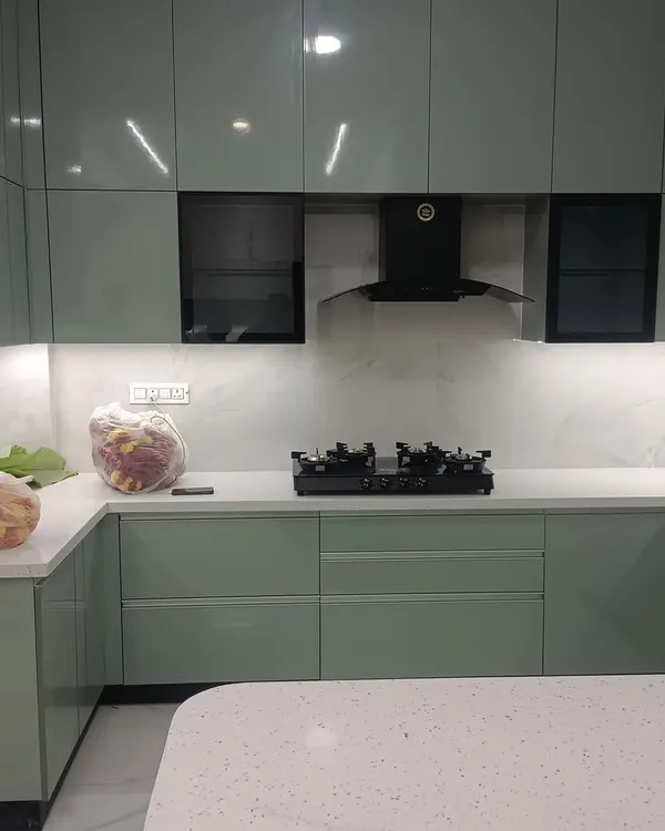 A wider view of the sage green modular kitchen, showing the U-shaped layout and the seamless integration of the breakfast counter. The quartz countertop and high-gloss cabinets reflect light, making the space feel bright and open.