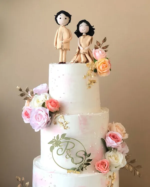 A close-up of the three-tiered engagement cake, showing the custom couple topper and monogram.