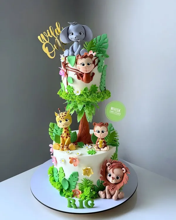 Go wild for this two-tiered jungle animal cake. This buttercream cake features adorable fondant animals like a lion, giraffe, and elephant, making it perfect for a "Wild One" first birthday.