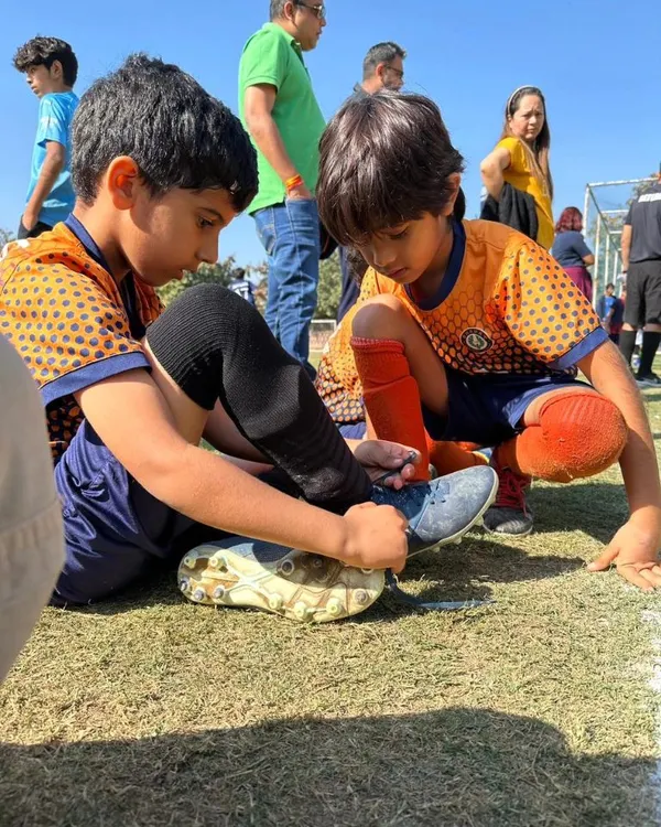 This is what teamwork looks like. A young player helps his teammate with his shoelaces, showing the camaraderie we build at our academy.