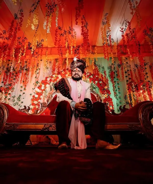A powerful, wide-angle portrait of the groom seated on a royal sofa. The dramatic lighting and grand decor create a regal and commanding presence, fit for a king on his wedding day.