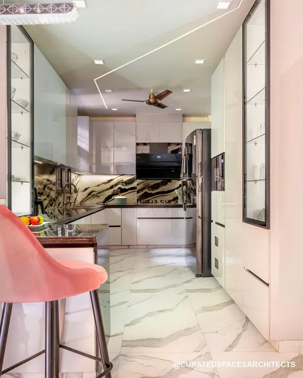 This kitchen was designed with a monochrome theme, featuring high-gloss white cabinets and a striking black and white marble backsplash. The rose pink breakfast chairs add a soft pop of color.