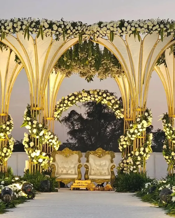 A magnificent wedding mandap with grand, petal-shaped arches adorned with white flowers and gold accents. This opulent design is perfect for a luxurious and unforgettable ceremony.