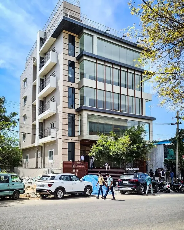 A street-level view of the completed commercial building in HSR Layout, occupied by brands like BlueStone. The design features a multi-level glass facade that creates a modern, transparent look for the office and retail spaces within.