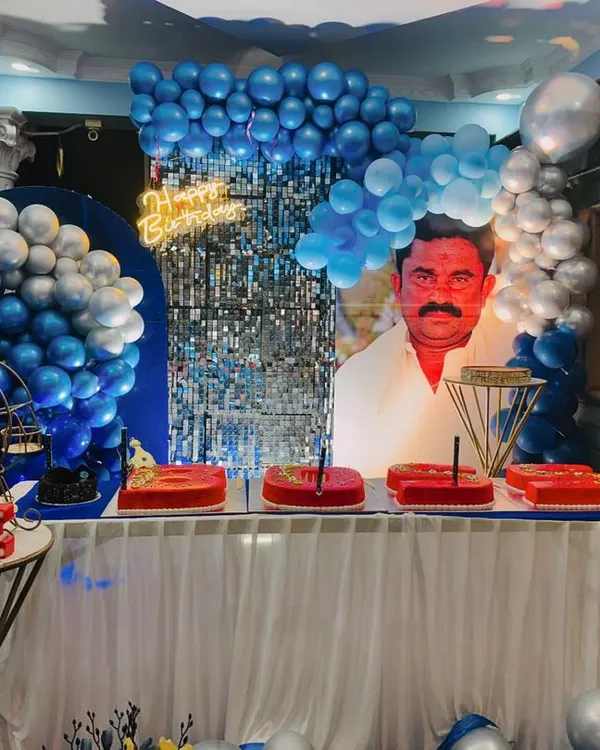 A full view of a highly personalized birthday setup. The key feature is the large custom portrait backdrop, complemented by a blue and silver balloon arrangement and a shimmer wall.