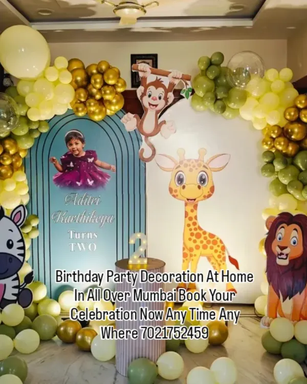 A cute jungle safari theme for a second birthday party at home. This setup features a custom arch backdrop, friendly animal cutouts like a lion and giraffe, and a green and gold balloon garland.