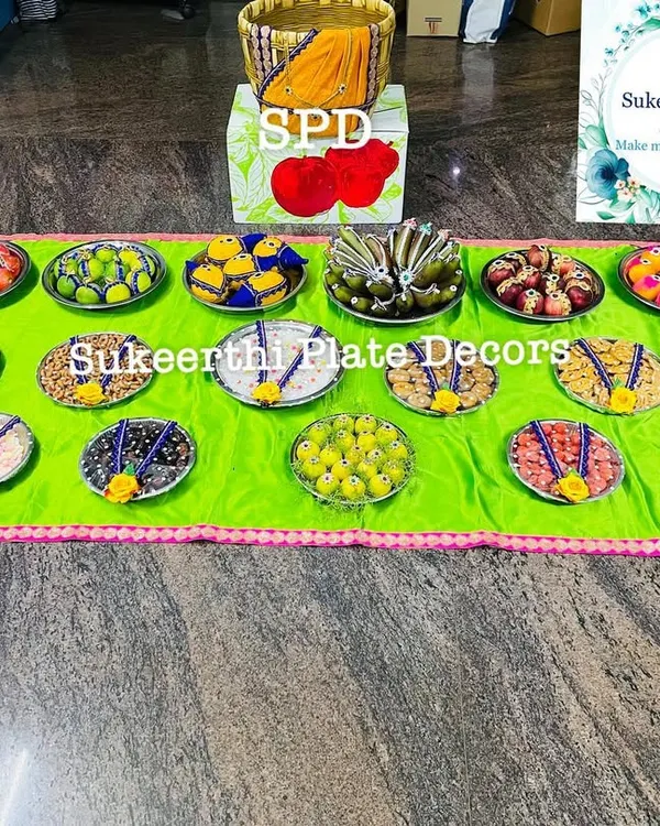 A large arrangement of seer plates filled with various sweets and savouries, ready for an engagement ceremony. The bright green cloth adds a pop of colour.
