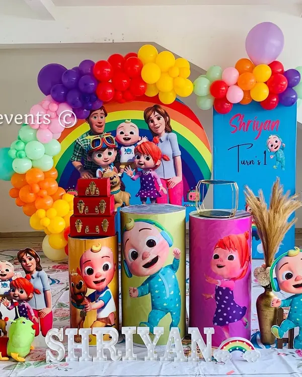 A vibrant and full Cocomelon theme for a first birthday. This setup is packed with characters, a rainbow balloon arch, and a light-up marquee number.