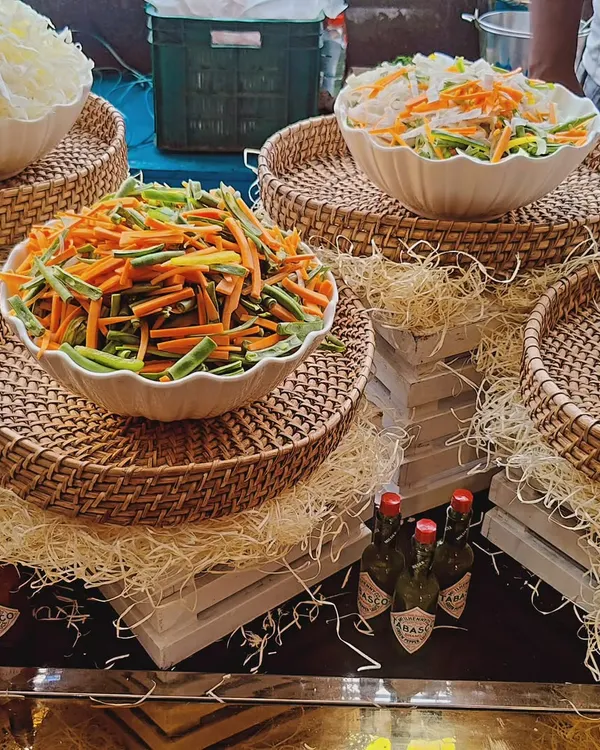 A display of our fresh salad ingredients, featuring bowls of julienned carrots, beans, and shredded cabbage. The rustic presentation with wicker baskets and straw shows our attention to detail in creating an appealing salad bar.