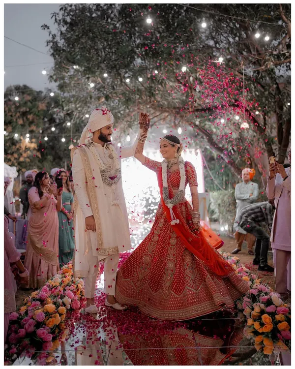 A magical moment from Miti and Dharmil's Gujarat wedding. The couple stands on a mirrored stage, showered with rose petals under a canopy of lights, creating a truly cinematic frame.