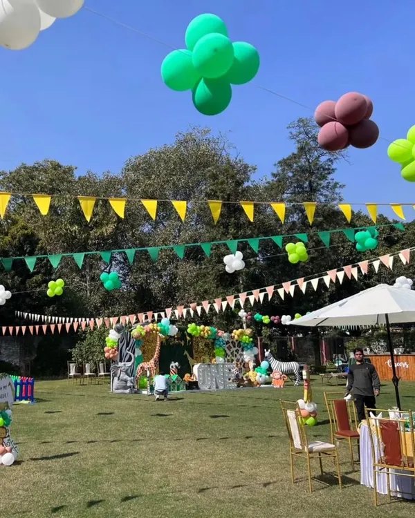 A wide view of a large-scale jungle themed party on a sunny day, showing guest seating, food stalls, and the main stage area.