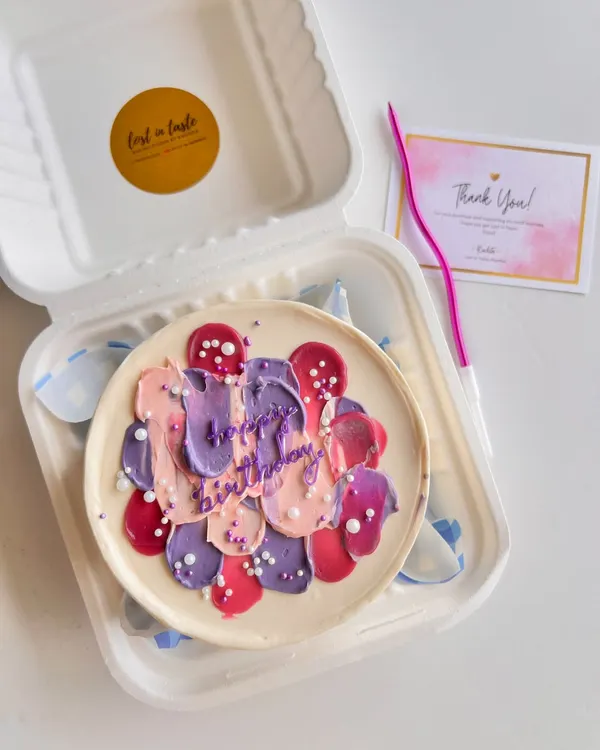 An abstract birthday bento cake featuring textured buttercream strokes in shades of purple, pink, and peach, finished with a sprinkle of white pearls for a modern, artistic feel.