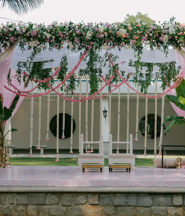A full view of the mandap for a South Indian morning wedding, featuring blush pink drapes, traditional jasmine and tuberose garlands, and sacred banana trees framing the stage.