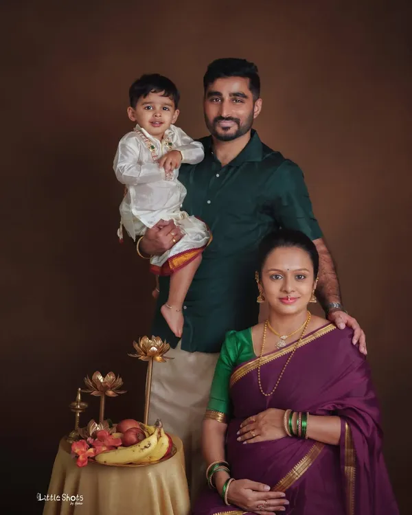 A beautiful family portrait with traditional South Indian attire. The family of three, with the young son held by his father, poses together in a classic studio setting.