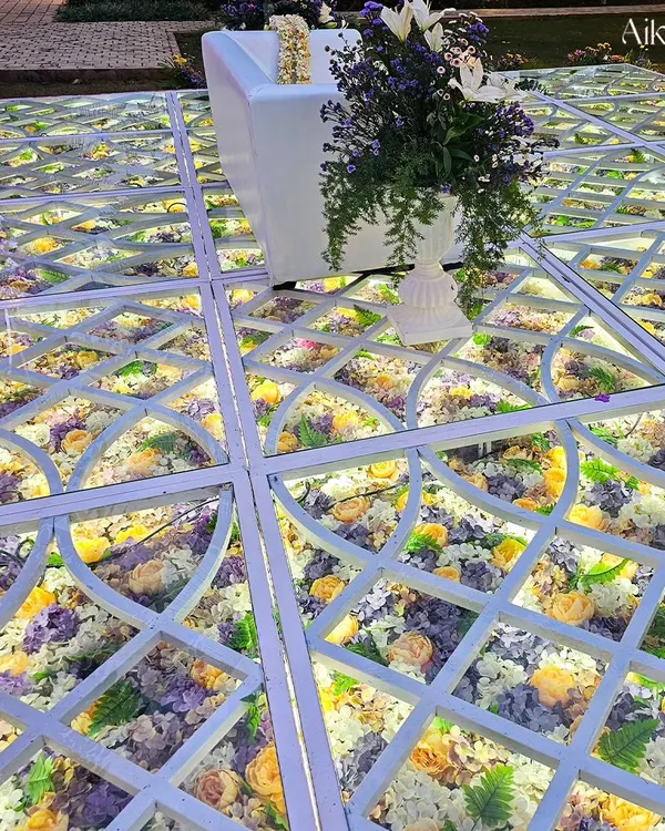A close-up of our signature illuminated glass floor, filled with a beautiful arrangement of yellow, purple, and white flowers. This detail adds a layer of luxury and enchantment to the wedding aisle.
