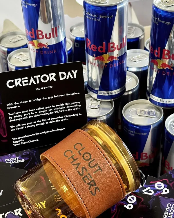 A high-energy PR hamper for 'Clout Chasers' featuring a custom-branded glass tumbler with a leather sleeve, Red Bull cans, and a branded event invitation. This is how we create gifts that perfectly match your brand's vibe.