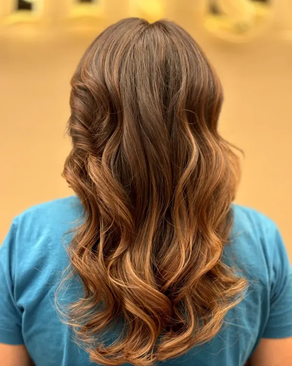 A stunning example of a balayage or ombré effect, with dark roots melting into lighter ends. The hair is styled in loose curls to perfectly showcase the color transition.