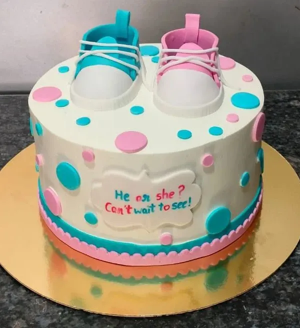 "He or she? Can't wait to see!" This is a classic gender reveal cake, decorated with pink and blue baby shoes and polka dots. The inside holds the sweet secret.