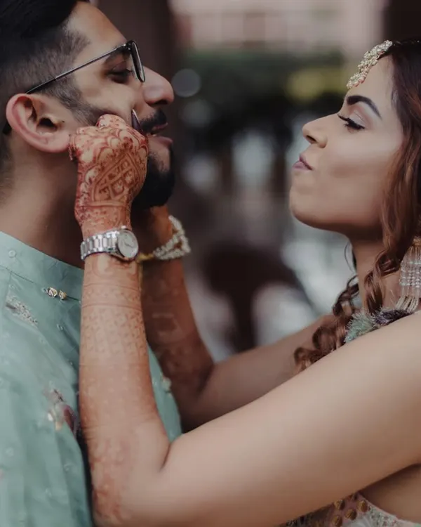 A playful moment between a bride and groom. The bride, with her hands full of henna, lovingly tweaks the groom's mustache, capturing their fun and affectionate relationship.