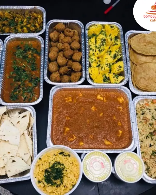 This is a typical spread for our bulk food delivery service. It includes a variety of our pure vegetarian dishes like Paneer Butter Masala, Dal, Dhokla, Puri, and Pulao, all packed and ready to serve.
