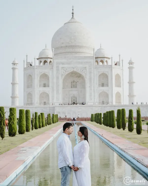 A classic, symmetrical shot of a couple at the Taj Mahal. Dressed in white, they complement the serene beauty of the monument, creating a powerful and iconic pre-wedding photograph.