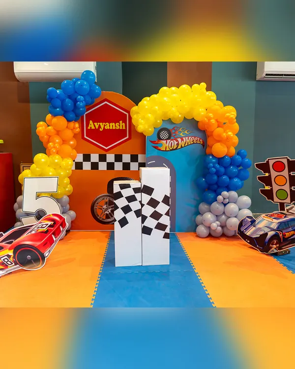The decor sets the stage for a high-speed adventure. This Hot Wheels party setup features a vibrant backdrop, car cutouts, and a race-track theme.